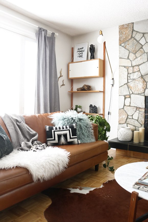 A brown couch with a white furry throw and a brown cowskin rug in a living room.