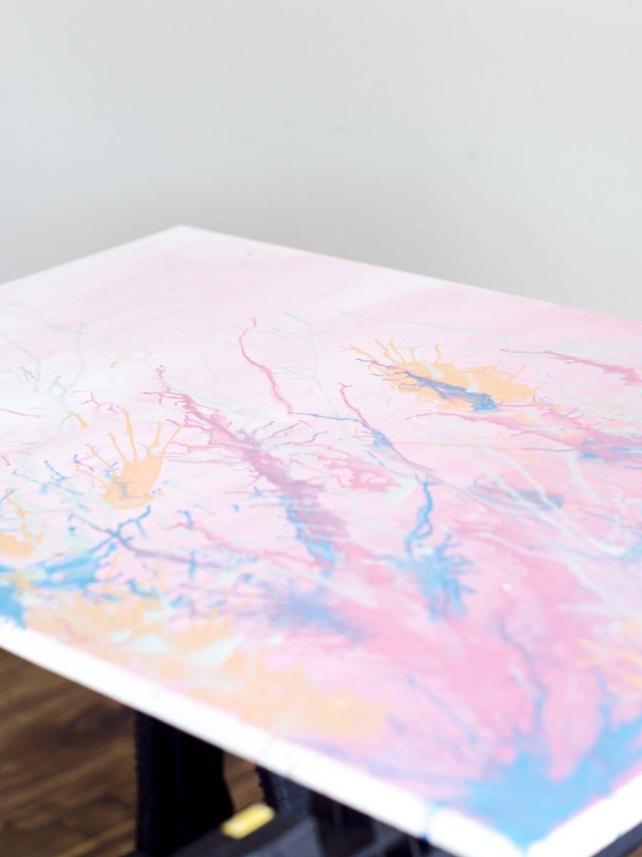 A mostly pink pastel piece of abstract artwork with a white border is laying flat.