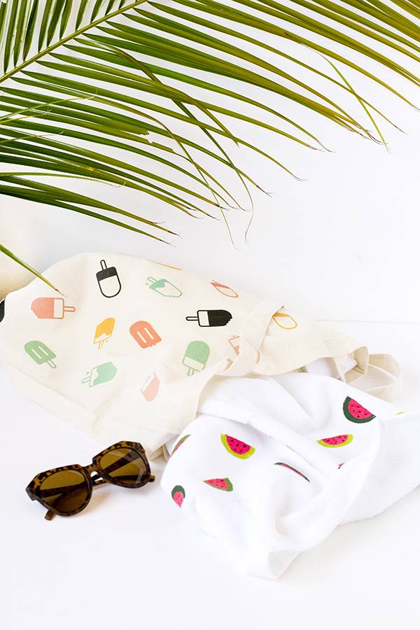 Sunglasses laying on a white table next to towels and a palm tree leaf.