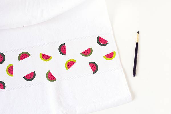 A paint brush lying near a white cloth on which watermelons are printed.