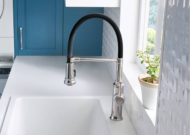 A black and silver kitchen sink faucet in front of a sunny window.