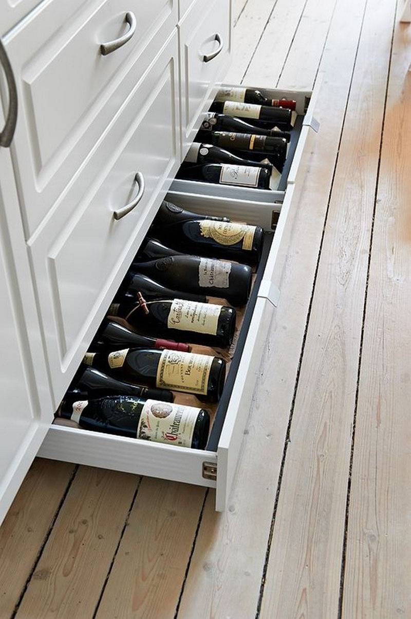 The bottom drawer of a long white dresser is full of wine bottles.