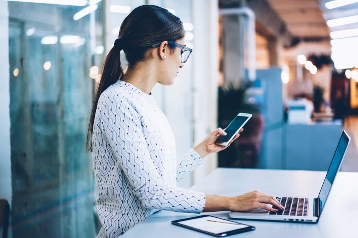 Woman looking at phone, sitting at computer