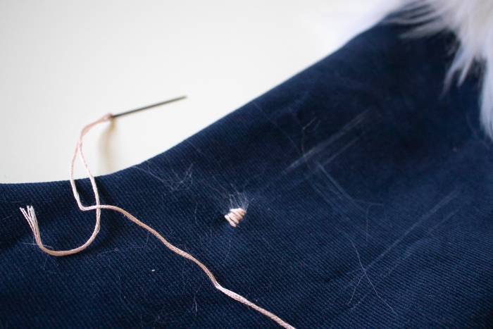 A needle, threaded with pink thread, on top of a blue stocking.
