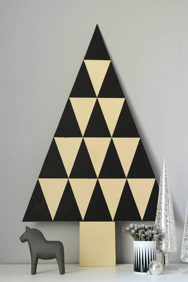 A gray wall with a triangle shaped piece of art with black and beige smaller triangles decorating it,  alongside small white Christmas tree, plant and horse figurine.