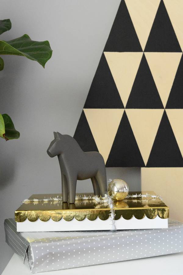 A gift box wrapped in golden paper having a horse toy at the top.