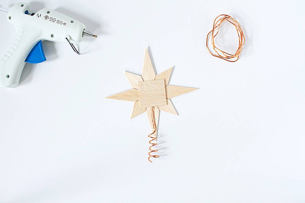 A hot glue gun rests next to some simple Scandinavian style ornaments that are handmade.