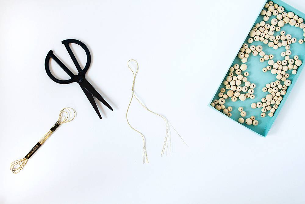 A blue tray holding white beads sits next to a pair of scissors and some thread.