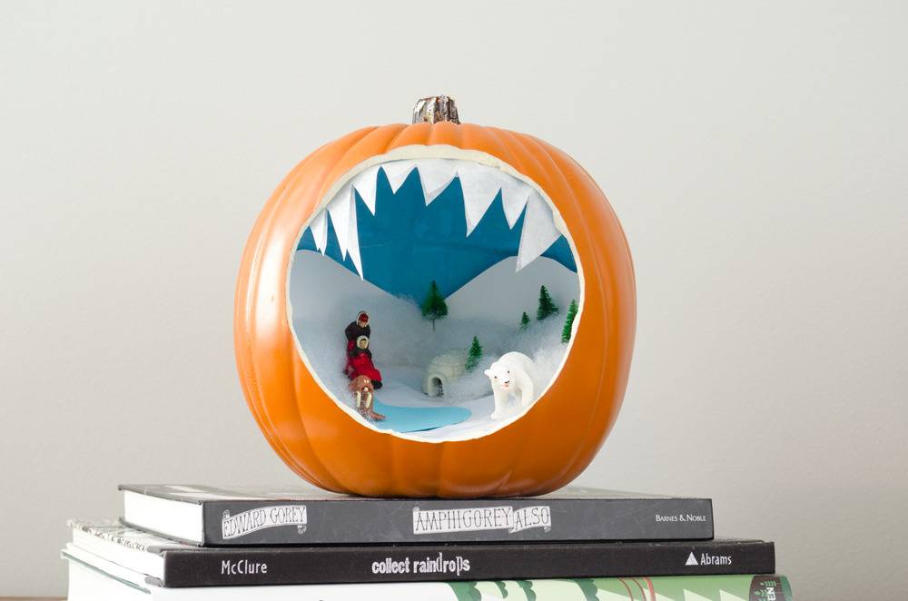 A sculpture of a jack-o-lantern  with a large hole that shows a winter scene inside.