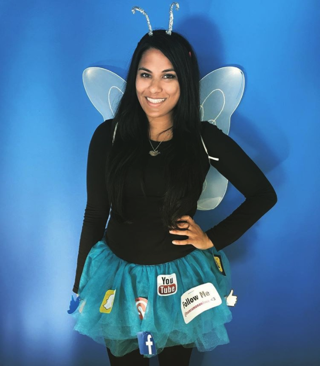 A woman is wearing a butterfly costume with a blue skirt, black top, wings on her back and antennae on her head.