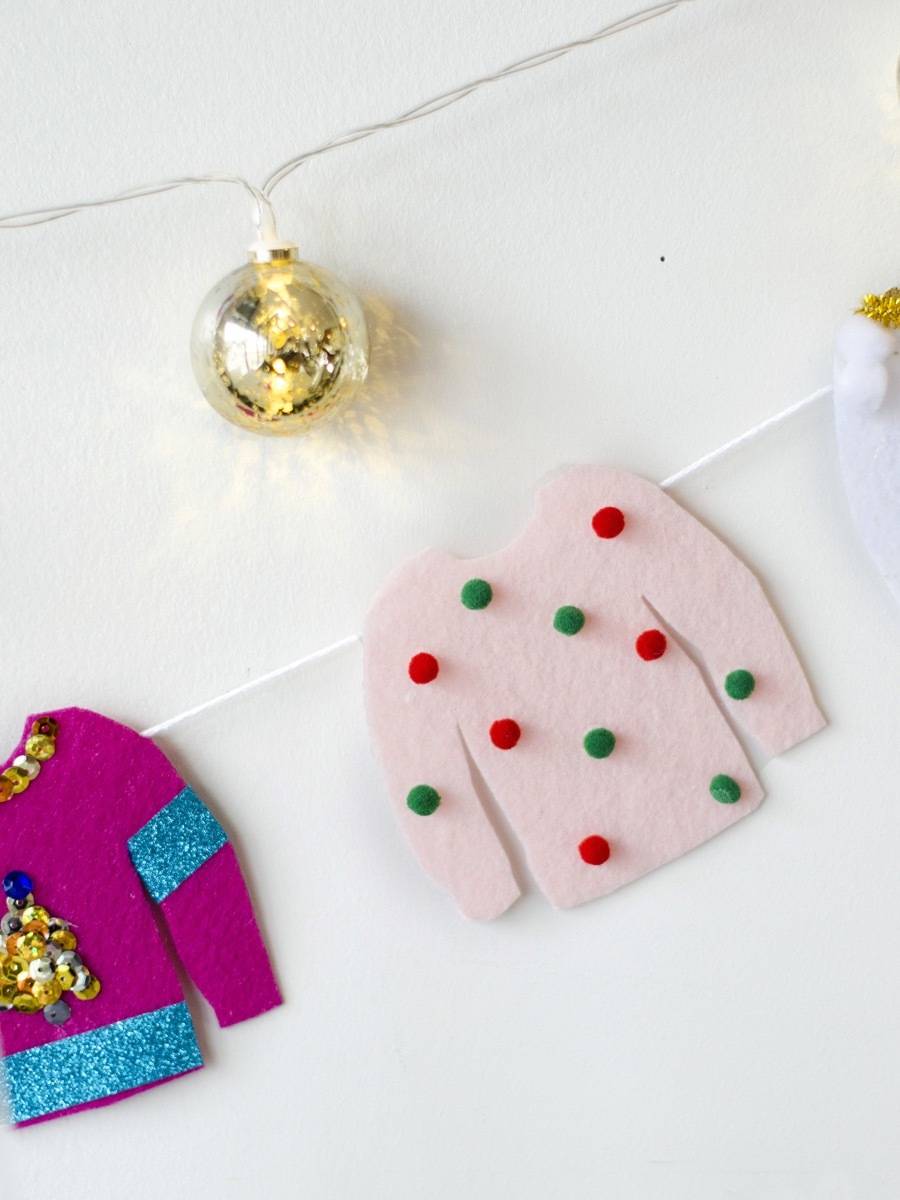 A gold ball on a string above a fuschia and blue sweater and a pink sweater with green and red polka dots on a string.