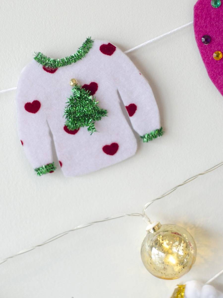 A small christmas sweater lays next to a golden ornament.