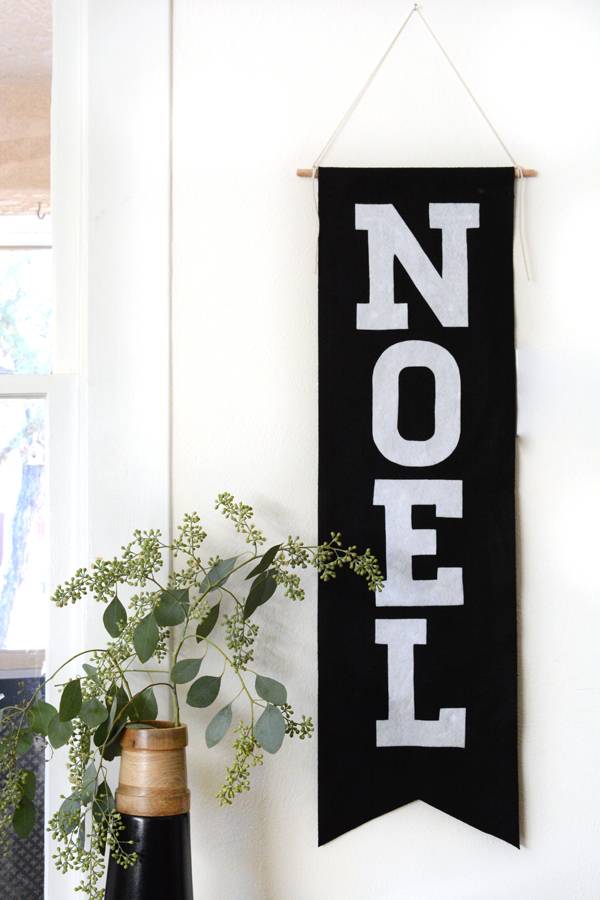 A black sign with the word Noel hangs near a plant.