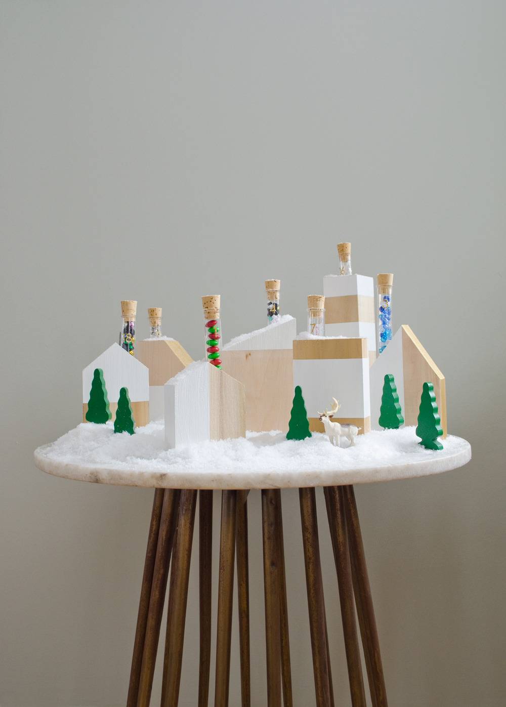 A Christmas village sits on a small table near a grey wall.