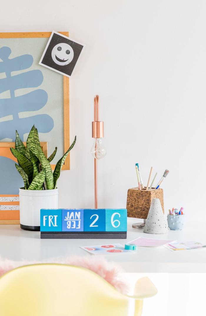 White desk with a blue wooden block calendar and green plant on it.