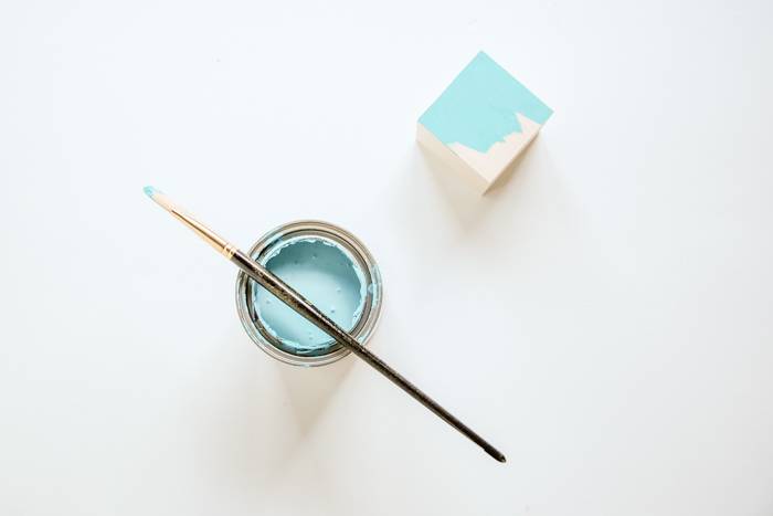 Paint brush is on the blue colored paint tin and half colored white cube on the white background.