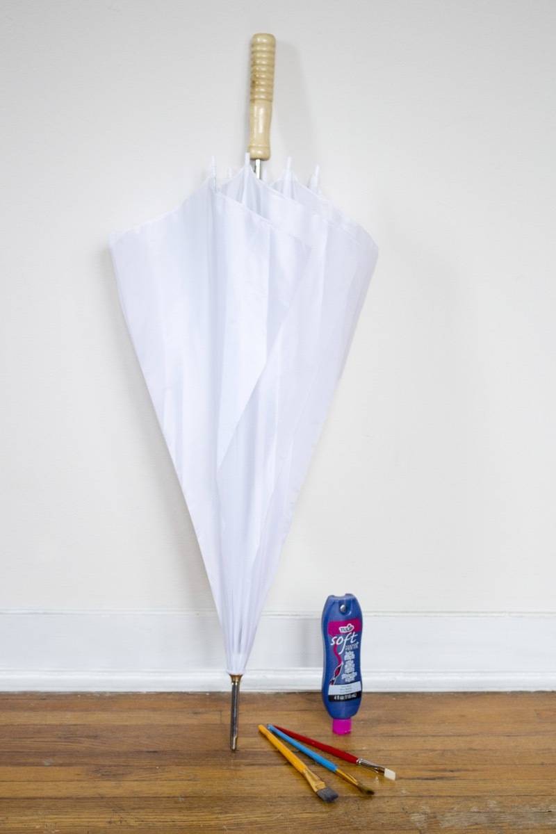 A white umbrella is leaning against a white wall near other items.