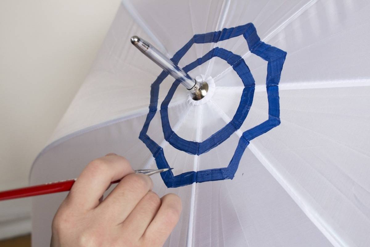 A person's hand painting on the top of an open umbrella.