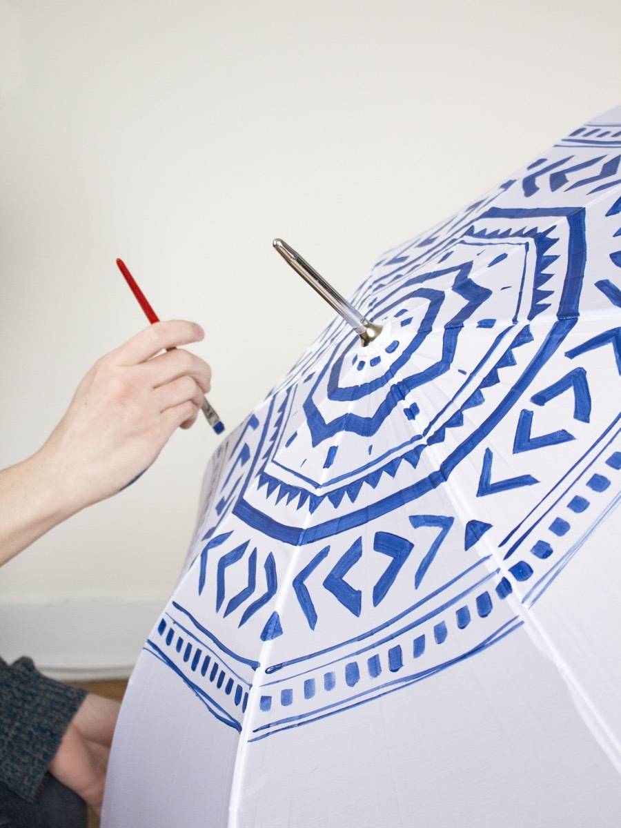 A person draws a blue design on an umbrella.
