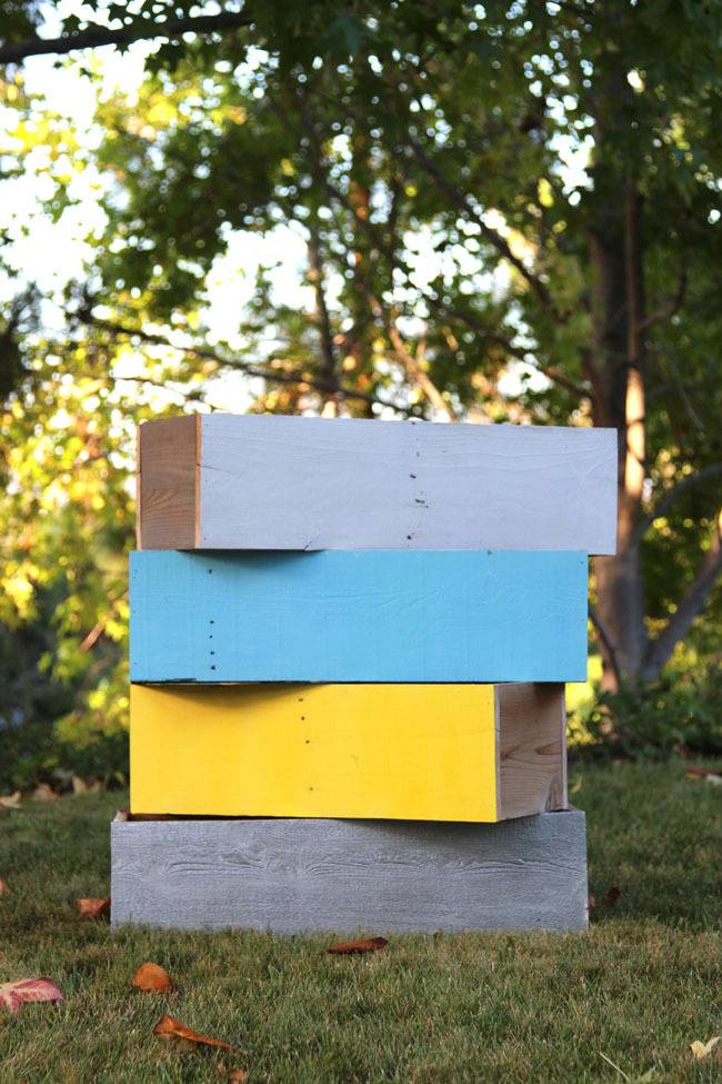 Do it yourself planters in gray, blue, and yellow are stacked on a lawn beneath a tree.