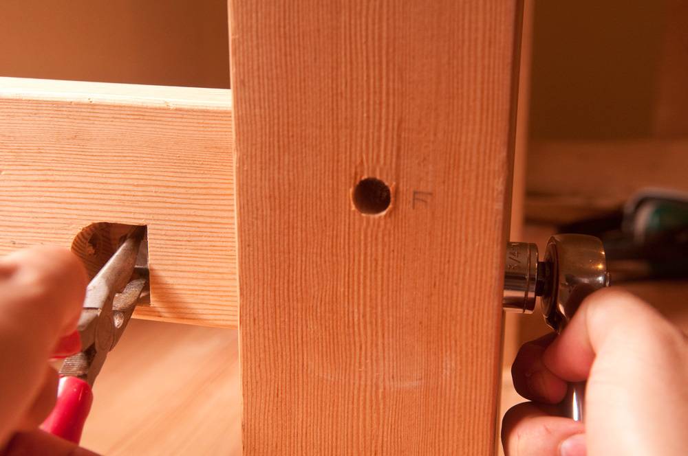 A person drilling a hole with a playa and a wrench in the wooden bench.