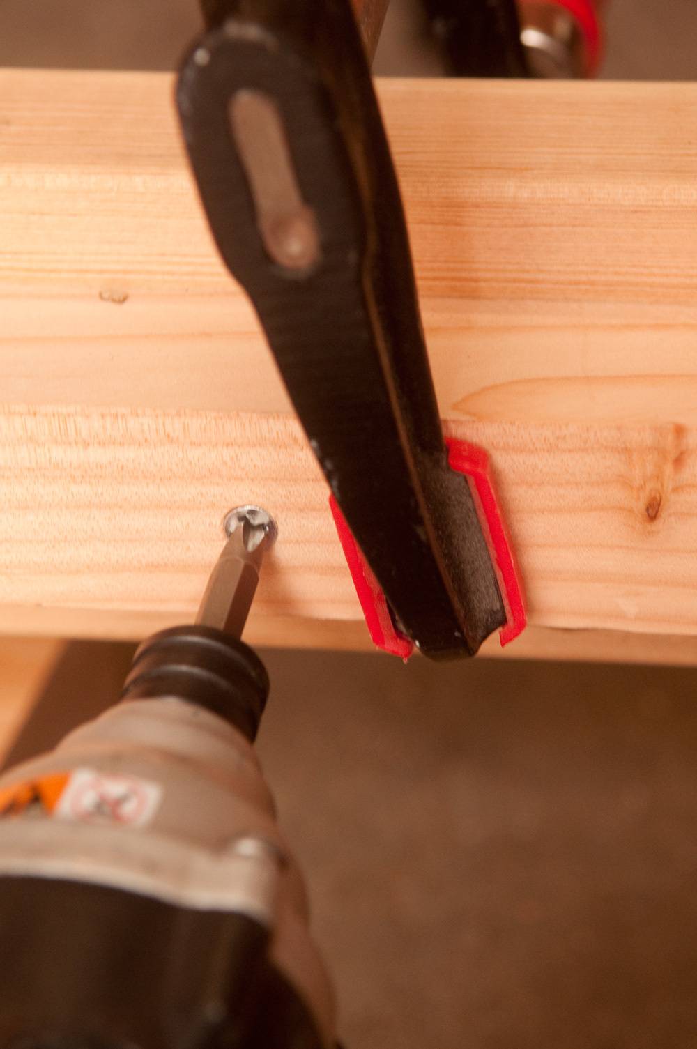 A drill head going into a screw on a board that is in a clamp.