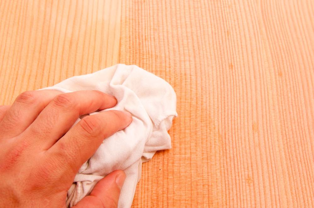 A hand holding a crumpled white rag is resting on a light wooden surface.