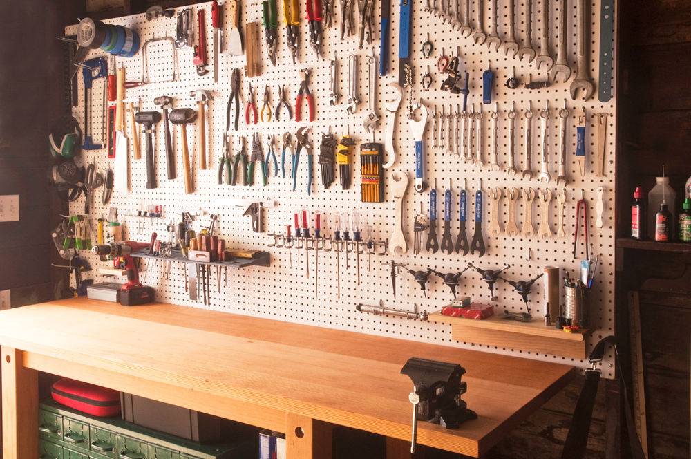 A pristine workplace, with a perfectley clean brown worktable and every tool hung in its place on the cork board above the table.