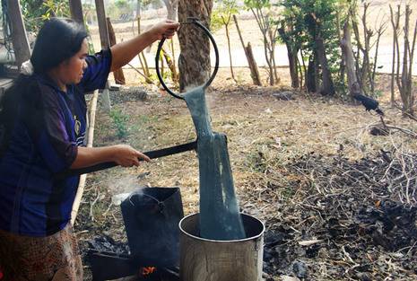 A person dipping something into a silver pot outside.