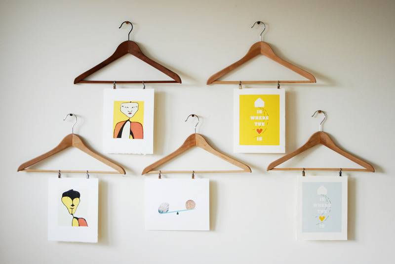 Six wooden hangers with artwork attached to each.