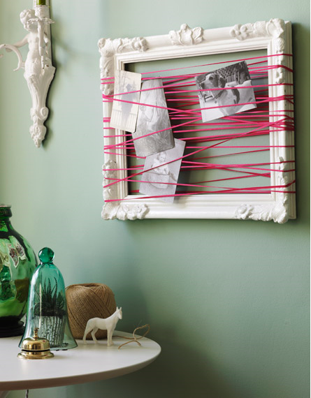 Pink string crosses over a white frame several times, while photos hang in the middle.