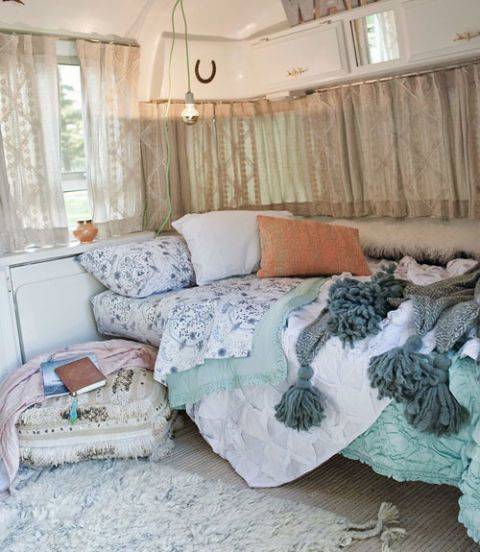 Small camper bed with light blue comforter and colorful pillows.