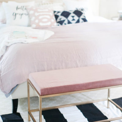 A bed with pink sheets on a black and white striped rug.