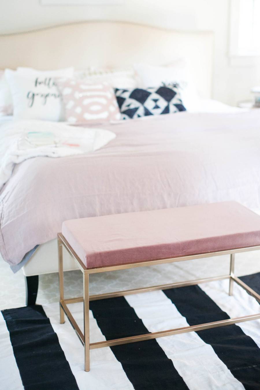 A bed with pink sheets on a black and white striped rug.