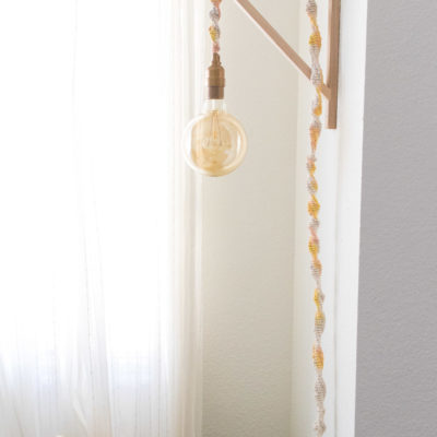 A large round slightly yellow light bulb hangs from a lamp that is hung over a bracket on the wall.