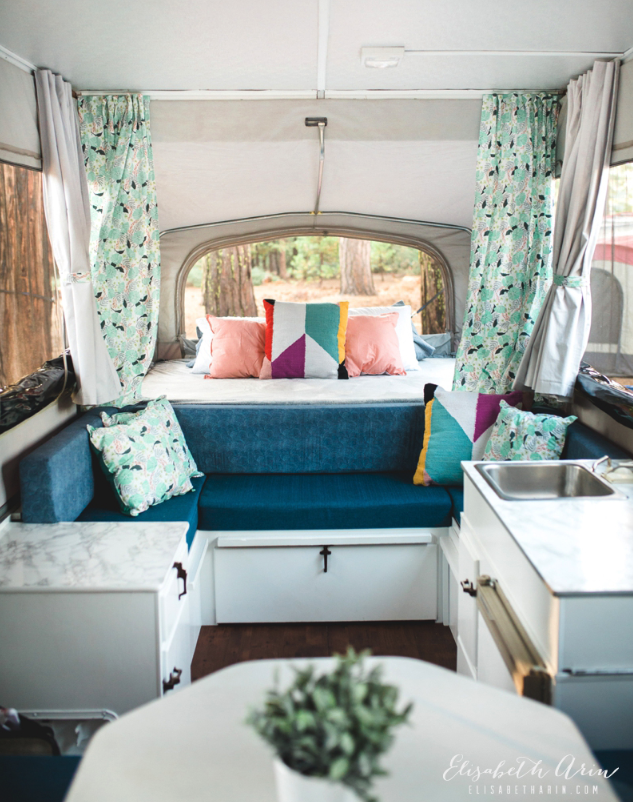 The interior of a camper with a sleeping area and green curtains.