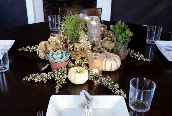 Mini pumpkins, and plants are used as a centerpiece on top of a black table for a holiday arrangement.
