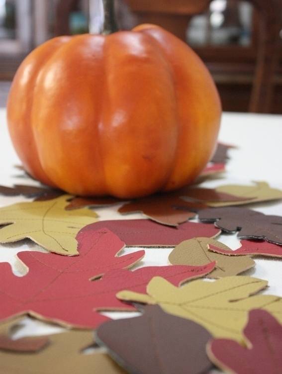 An orange pumpkin on a table with paper fall leaves