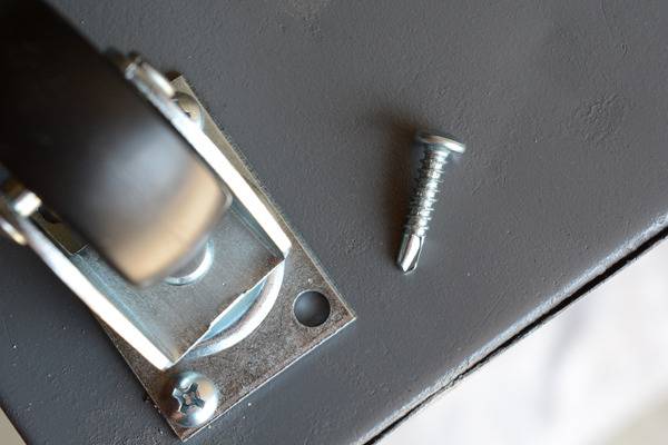 A screw needs to be screwed back into a roller at the bottom of a piece of furniture.