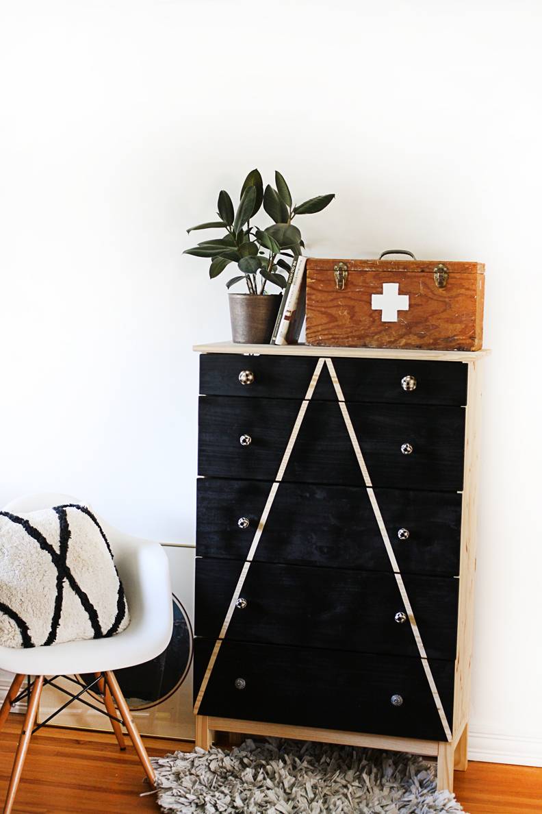 Black wooden drawer set pressed up against a wall with a plant wooden basket sitting on top of it.