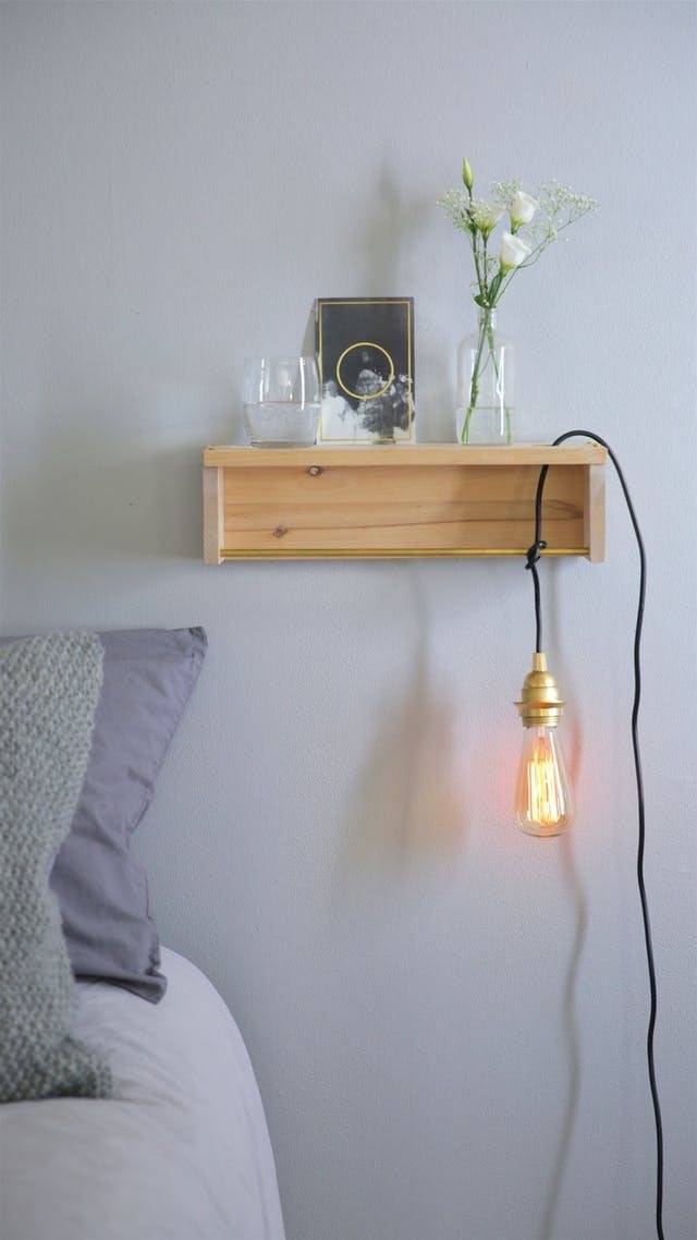 A light hangs down from a shelf near a bed.