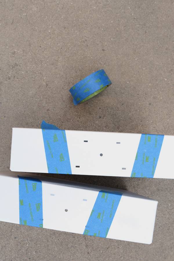 Two white blocks with blue painters tape in a v shape sit on the floor