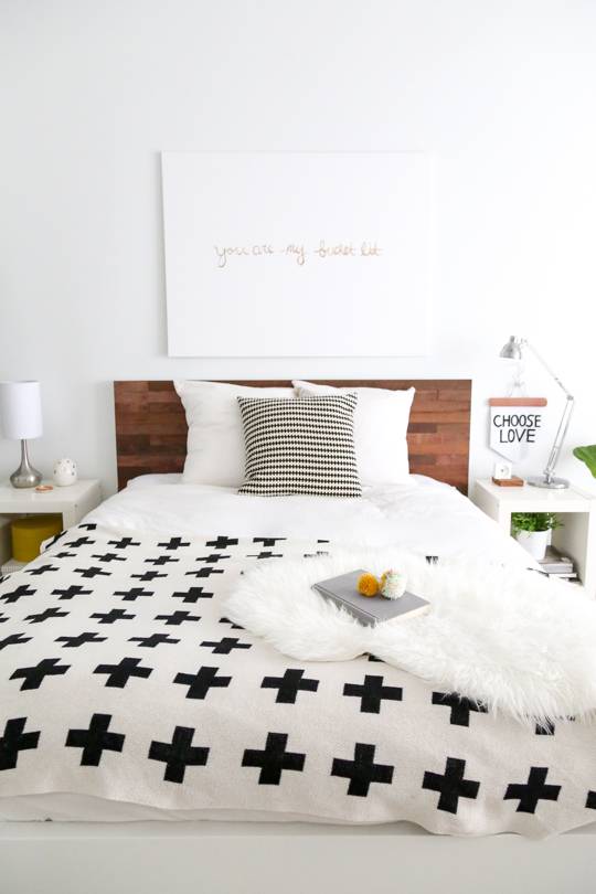 A white bedroom has a large, white bed with black crosses on it.