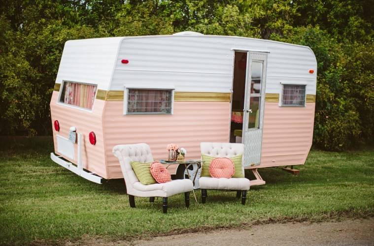 A white and pink camper with two chair lying on the ground.