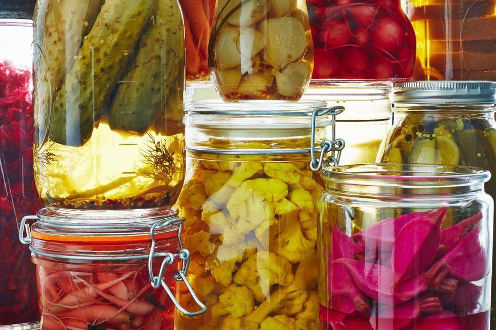 Jars of picked cucumbers, carrots, onions and other vegetables are stack on top of one another.