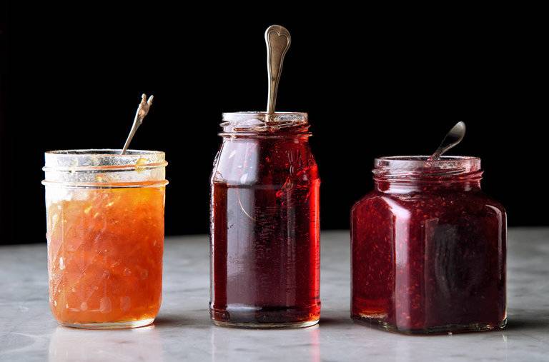 Three open glass jars of jam with spoons in them.