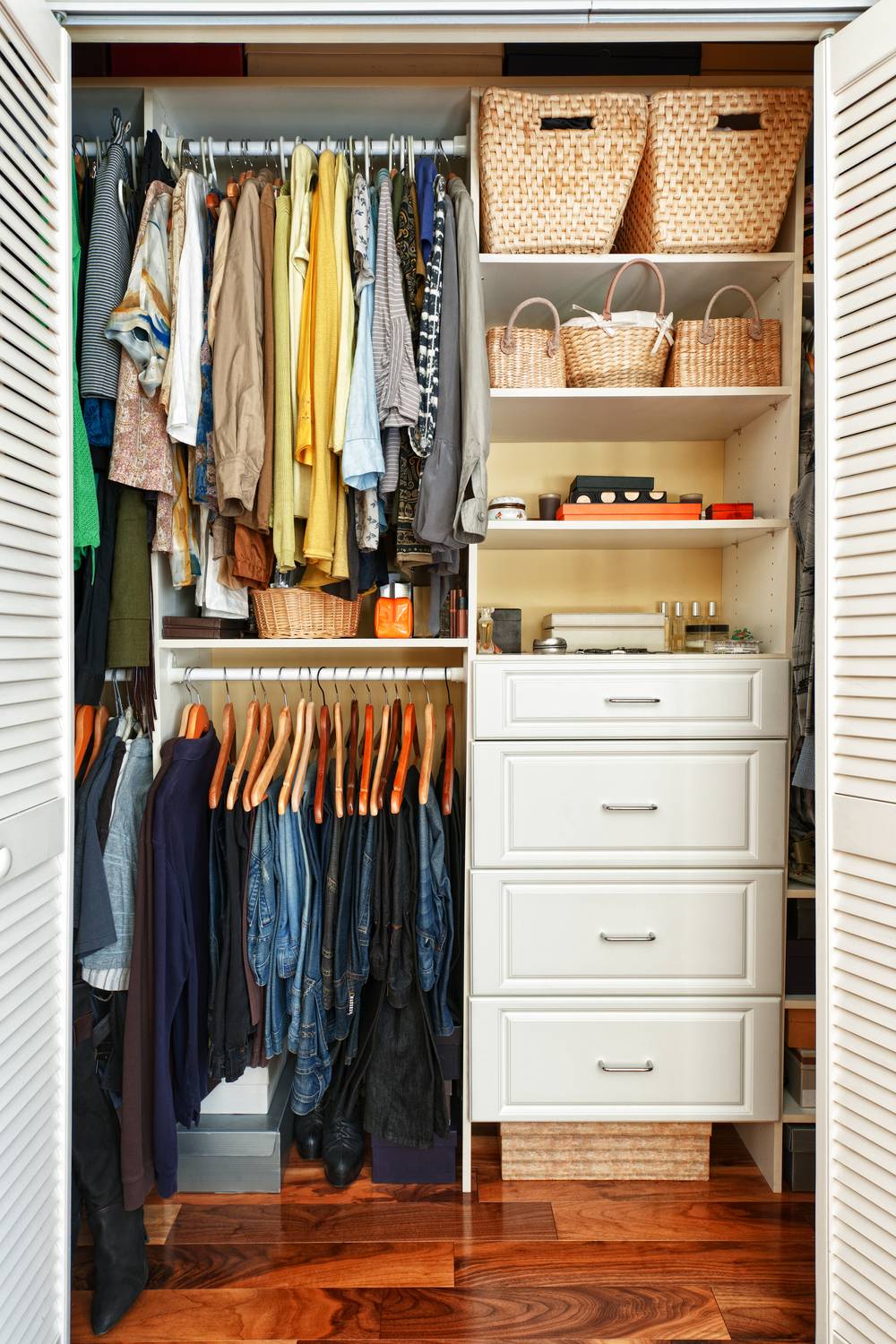 A well organized closet with hanging clothes and white drawers.