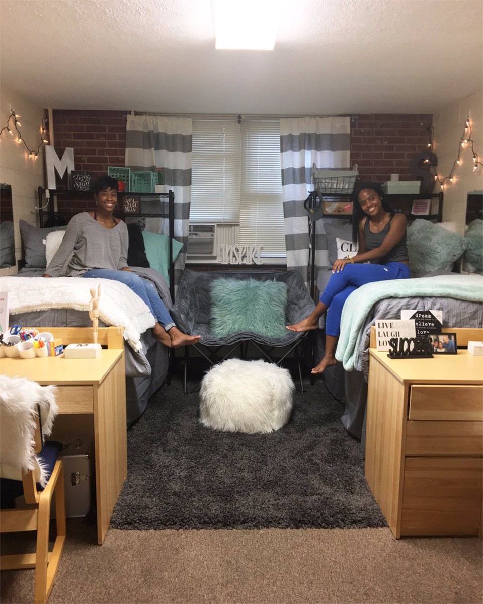 Two roommates sitting on two bed in a small dorm.