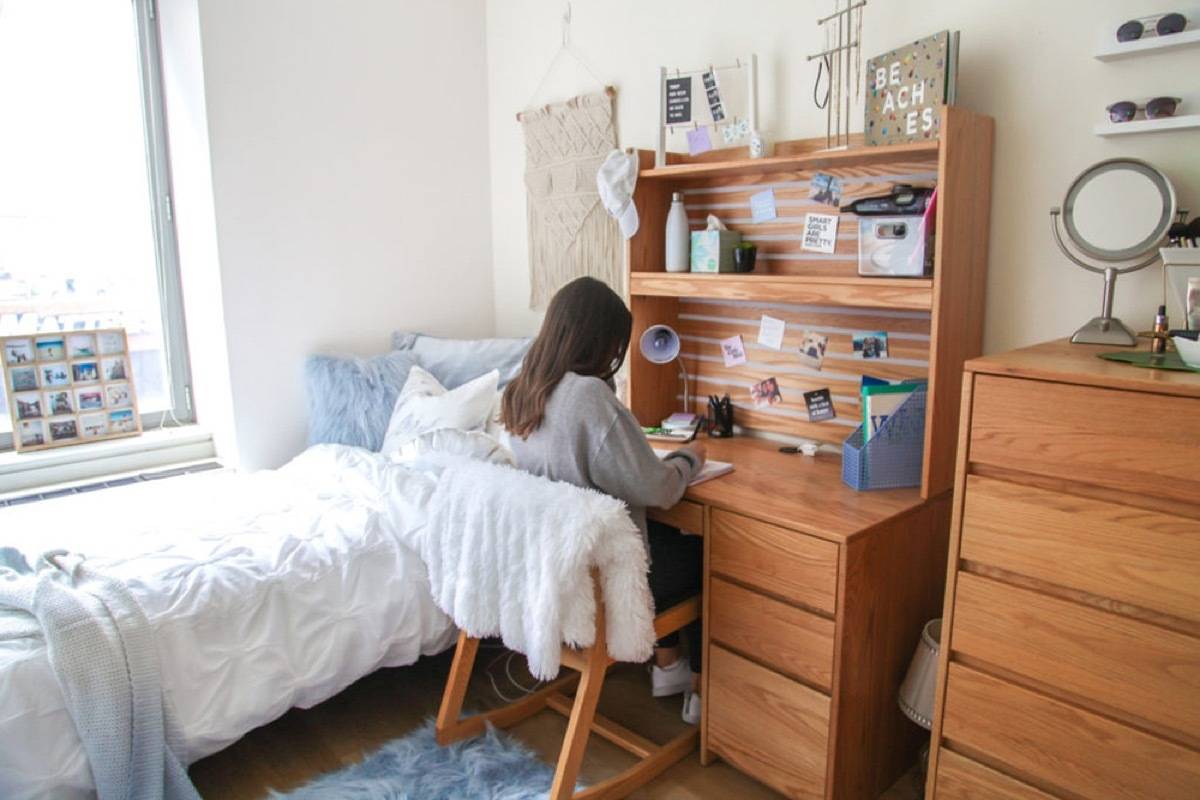 A girl sits at a wooden desk with shelves in her bedroom.