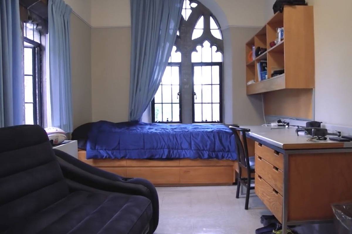 Room having a wooden table, chair and a bed having blue bedsheet.